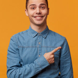 Home Smiling man wearing a light blue denim shirt pointing to the side.